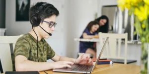 Student wearing a headset with microphone while using a laptop for online learning at home
