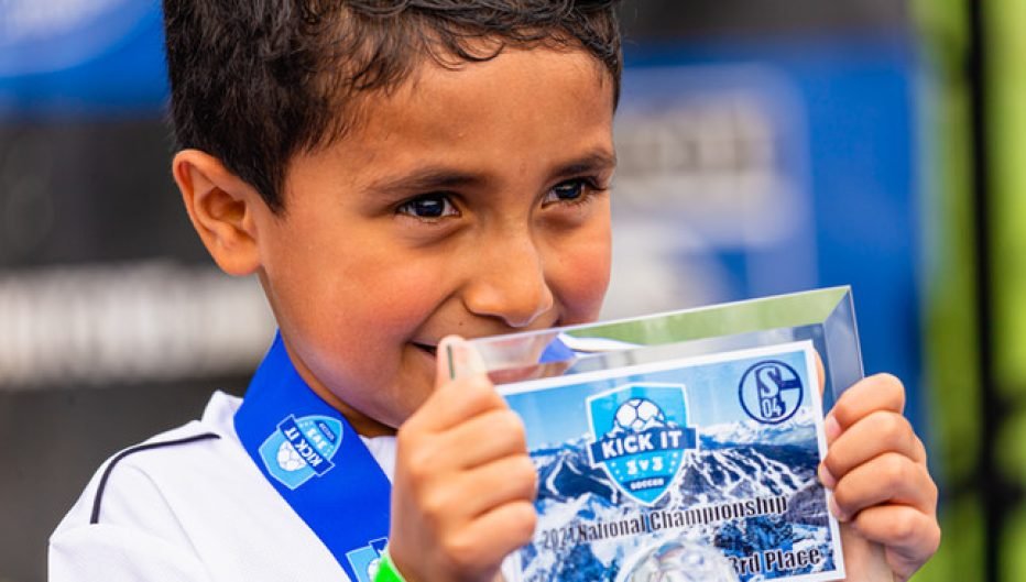 Young Kick It 3v3 Soccer participant wearing a medal and holding a first-place award plaque at the 2024 National Championship event
