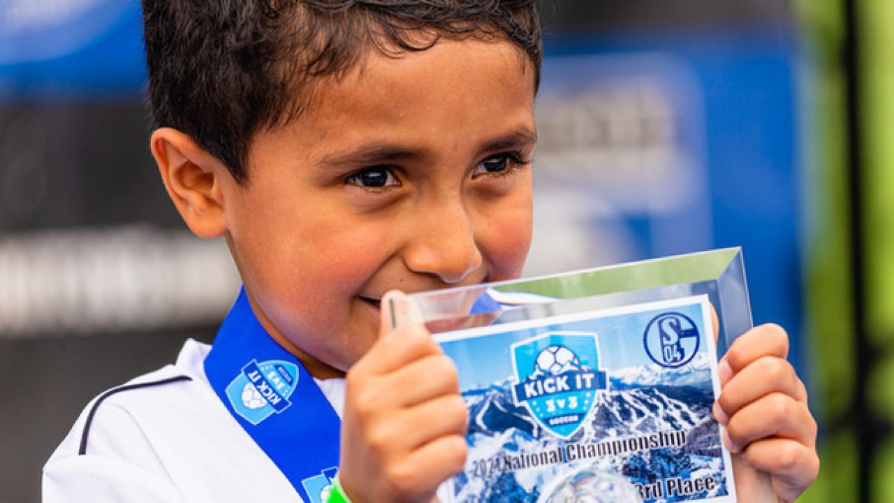 Young Kick It 3v3 Soccer participant wearing a medal and holding a first-place award plaque at the 2024 National Championship event