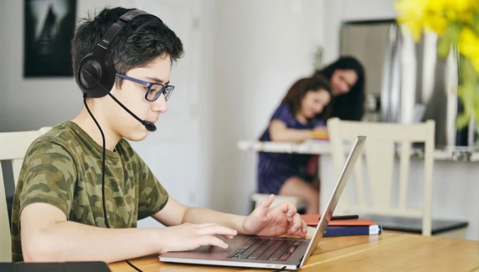 Student wearing a headset with microphone while using a laptop for online learning at home