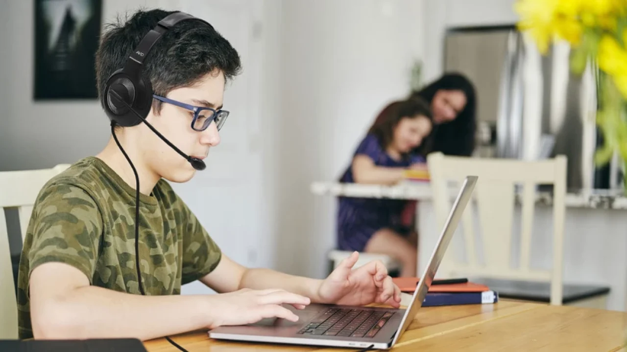 Student wearing a headset with microphone while using a laptop for online learning at home